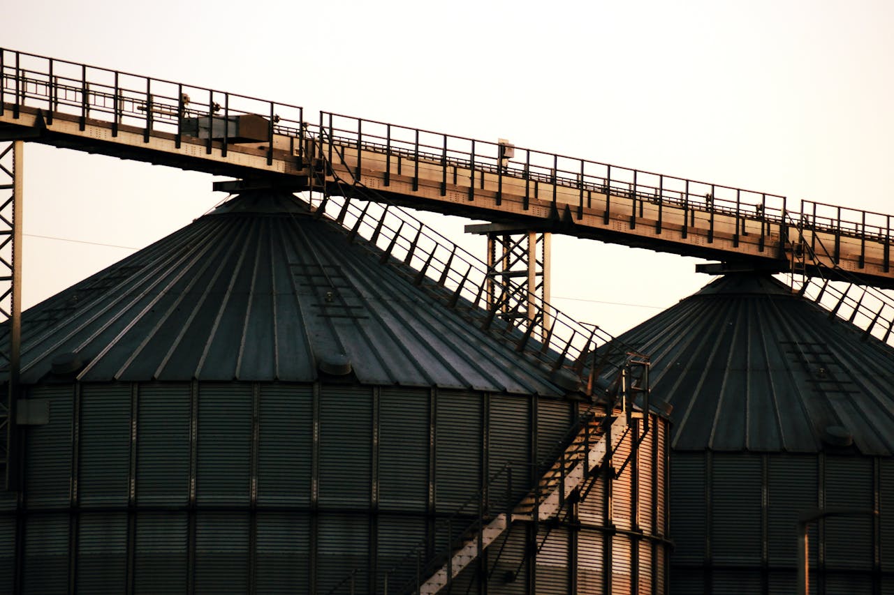 services-05 Close-up image of industrial grain silos with overhead walkway at sunset, conveying modern industry.