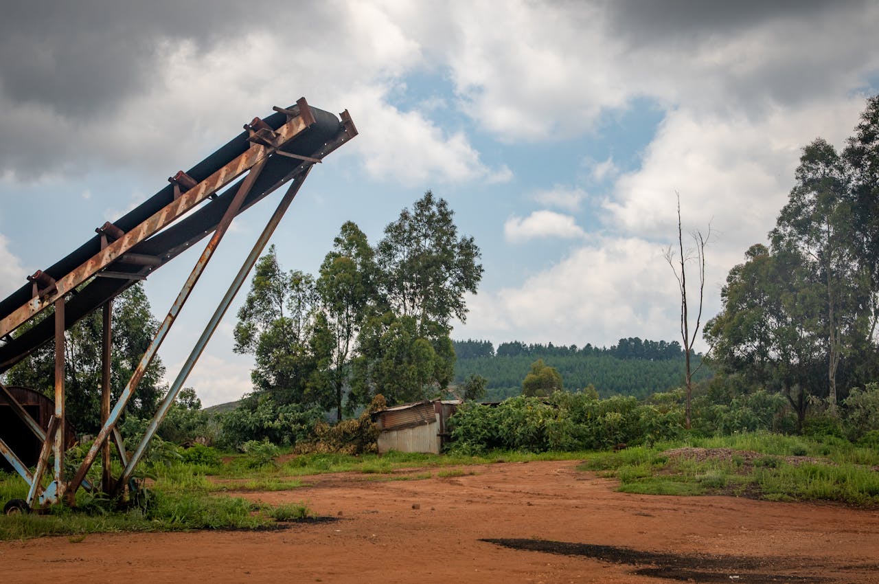 why-choose-us Abandoned conveyor belt amidst rustic rural landscape under cloudy summer sky.